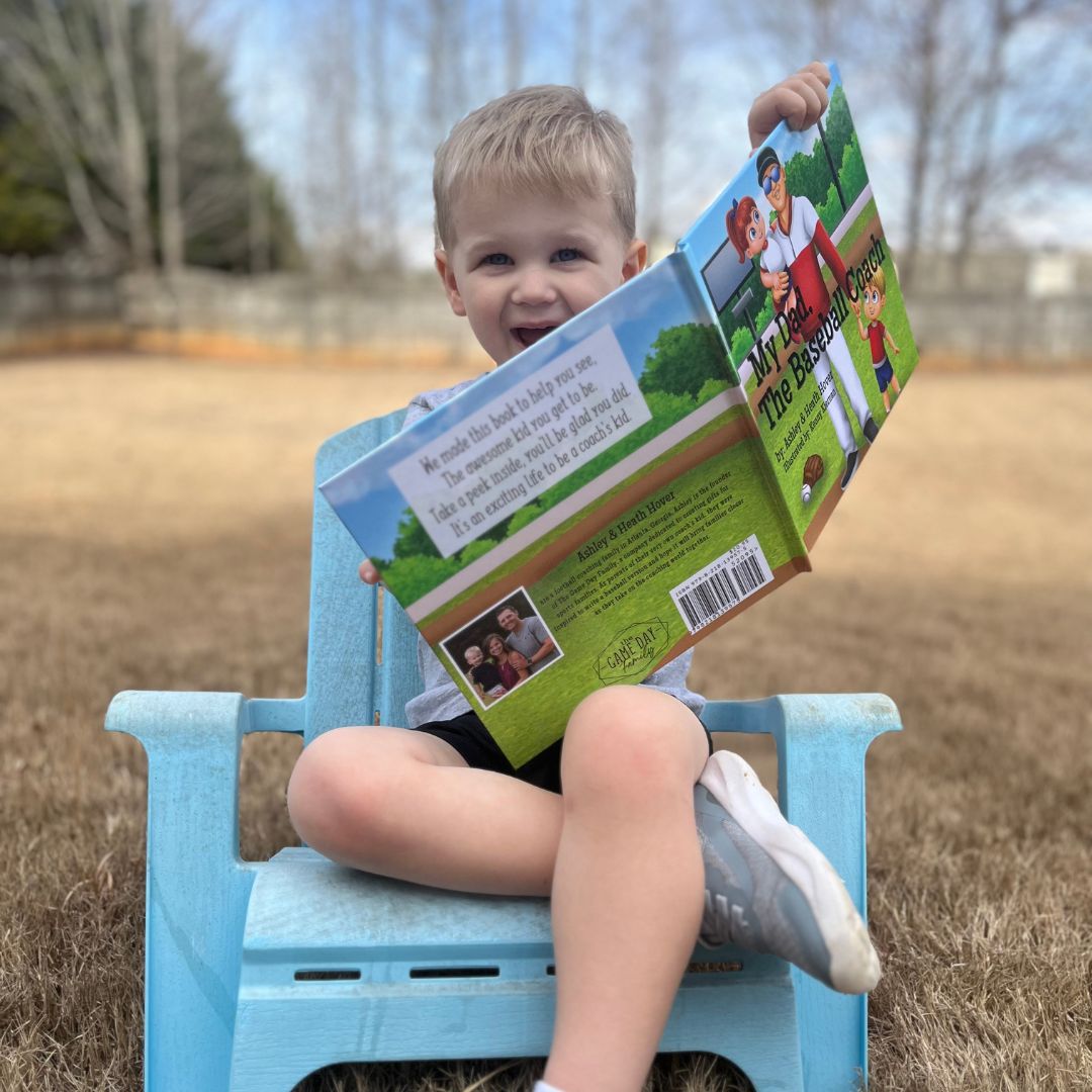 kid enjoying looking at a book showing off his dad as a baseball coach